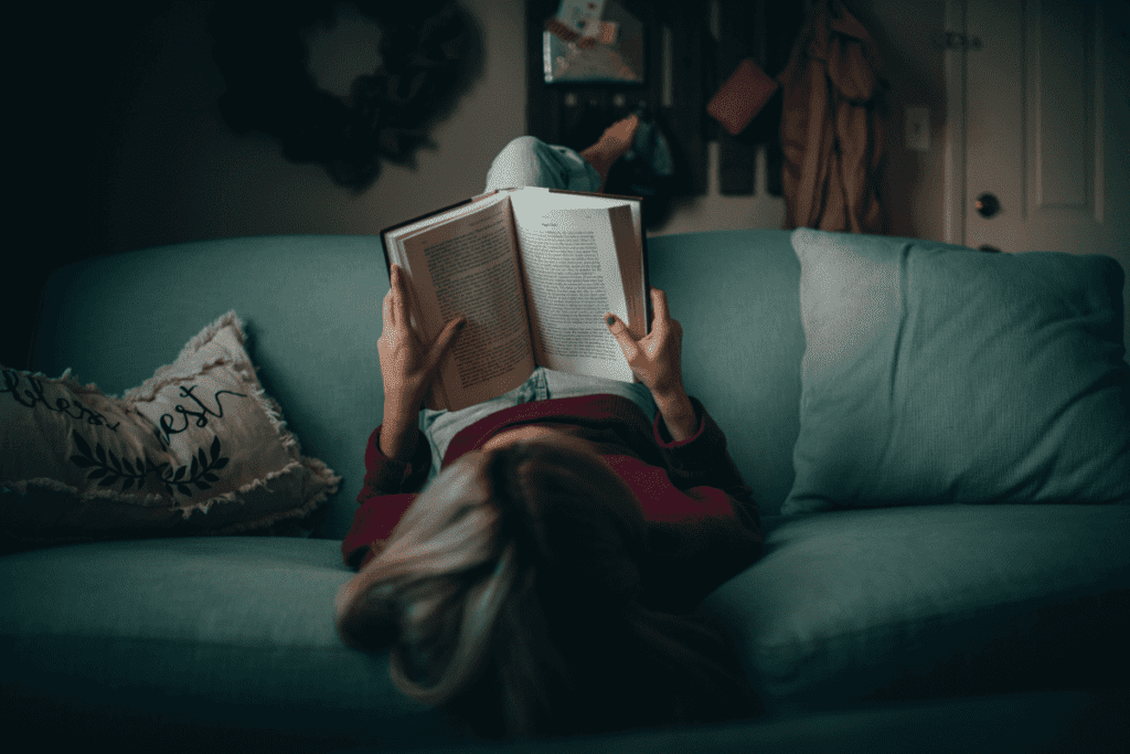 Woman laying upside down on a couch reading an open book.