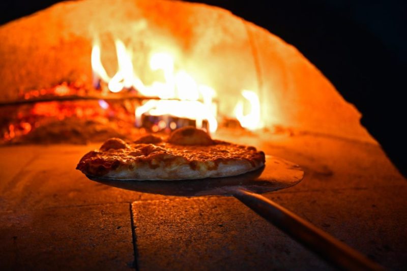 A pizza going into a wood fired oven.