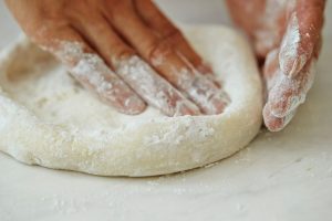 A person pressing pizza dough on a white surface.