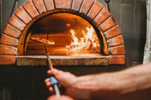 A person putting a pizza into a wood fired oven.